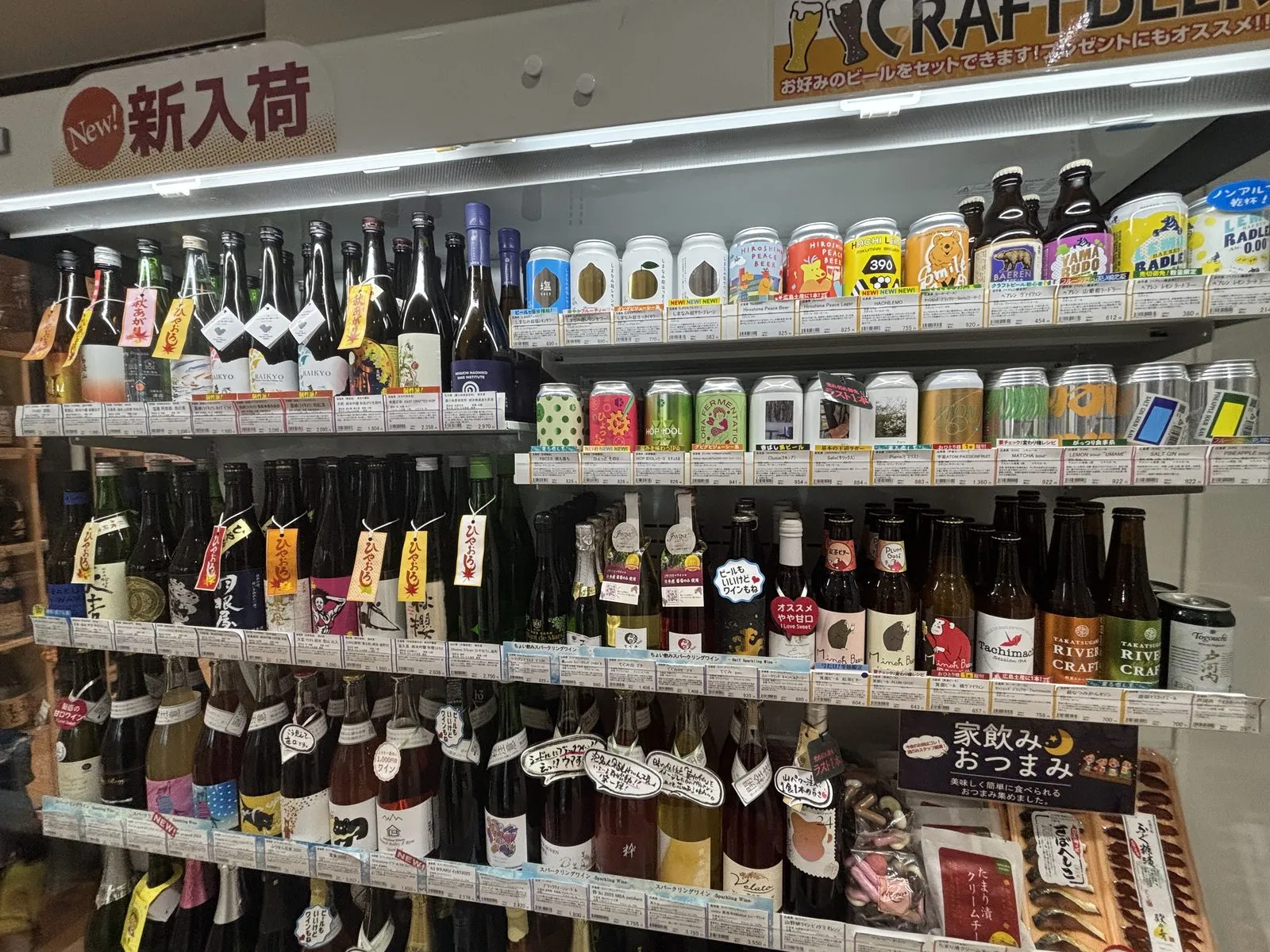 新入荷の棚。日本酒の瓶とカラフルなクラフトビールの缶がぎっしり並ぶ