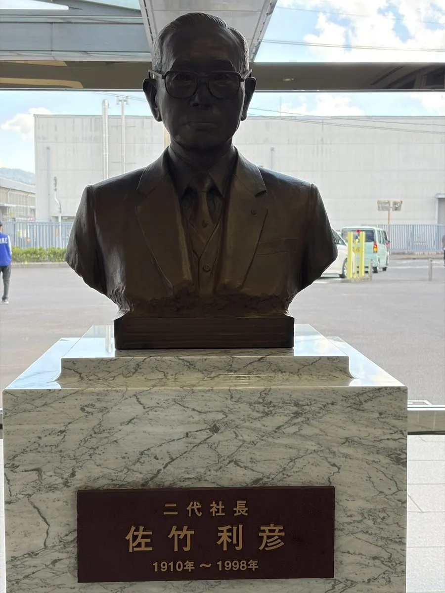 サタケ本社の入口に立つ二代社長・佐竹利彦の胸像。台座に1910年から1998年の銘板