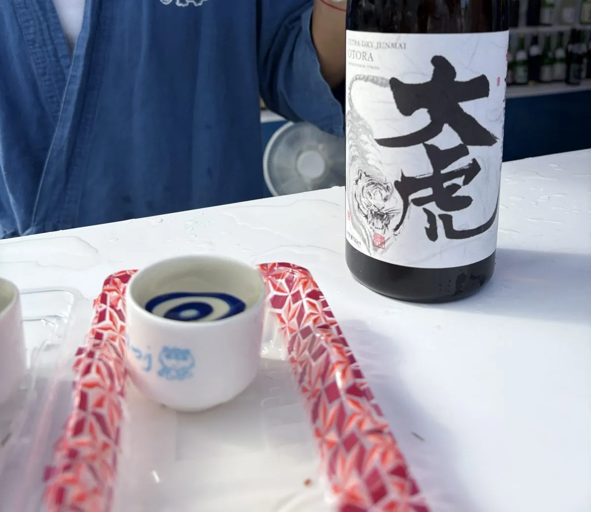 大虎の瓶。ラベルに「EXTRA DRY JUNMAI」の文字。手前に酒まつりの猪口と、赤い模様の受け皿